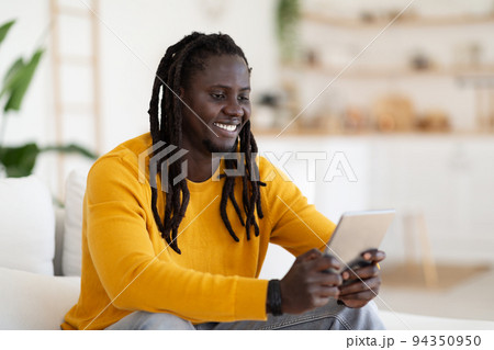 Cheerful Black Man Playing Game On Digital Tablet While Relaxing At Home Cheerful Black Man Playing Game On Digital Tablet While Relaxing At Home 94350950