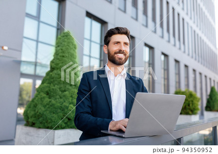 Cheerful confident handsome young caucasian guy with beard in suit typing on laptop Cheerful confident handsome young caucasian guy with beard in suit typing on laptop 94350952