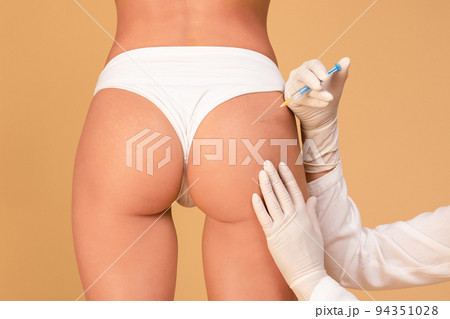 Butt lifting concept. Back view of slim woman having hip injection at beauty salon, closeup, beige studio background Butt lifting concept. Back view of slim woman having hip injection at beauty salon, closeup, beige studio background 94351028