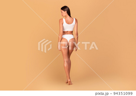 Bodycare concept. Back view of slim lady standing in white panties and top bra underwear over beige background 94351099