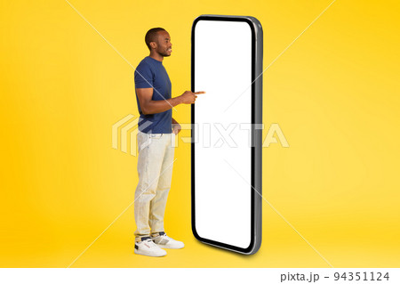 African American Male Using Large Smartphone Empty Screen, Yellow Background 94351124