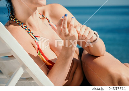 Woman in rainbow bikini. Happy tanned well looking middle aged woman in rainbow swimsuit at seaside, blue sea water in background. Holiday, vacation and recreational concept. 94357711