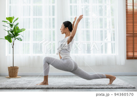 Happy Athletic Asian woman practice yoga stretching pose for stretching muscle for warm up with meditation smile,Healthy female doing yoga exercise and relax at home. Yoga self care Healthcare Concept 94360570