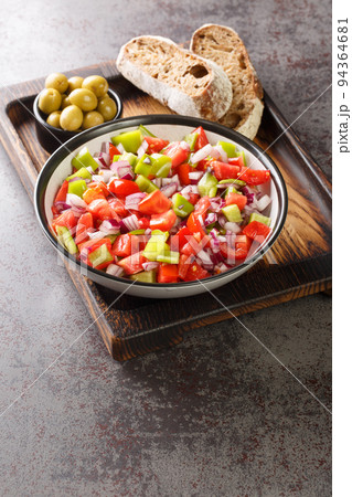 Salad of bell green peppers, tomatoes and onions served with olives and homemade bread close-up on a wooden board. Vertical 94364681