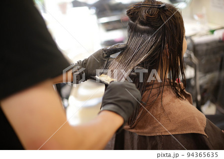 女性の髪に薬剤を塗布する男性美容師 94365635