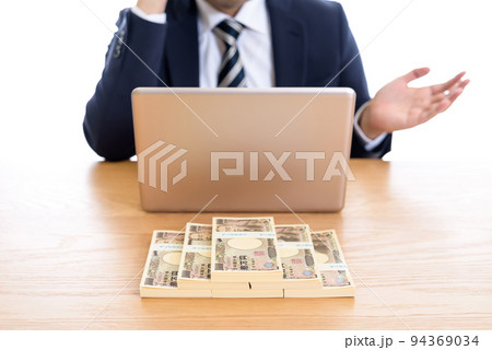 ノートパソコンと百万円の札束を並べた前でポーズをとるビジネスマン　日本円 94369034