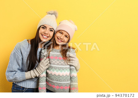 Happy mother and daughter in warm clothes on yellow background, space for text. Winter vacation 94370172