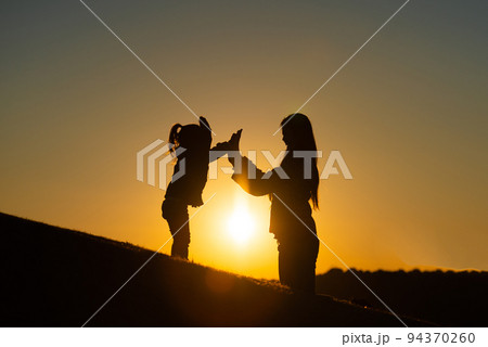 夕暮れの野原で遊ぶ親子のシルエット 94370260