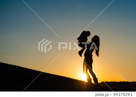 夕暮れの野原で遊ぶ親子のシルエット 94370261