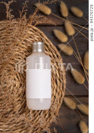 Cosmetic bottle with blank label on boho wattled placemat near Hare's Tail grass, Mockup Cosmetic bottle with blank label on boho wattled placemat near Hare's Tail grass, Mockup 94370729