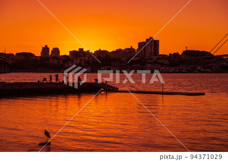 People on pier with sunset sky and reflection on water in Florianopolis People on pier with sunset sky and reflection on water in Florianopolis 94371029