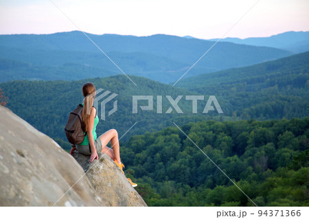 Tired hiker girl relaxing on rocky mountain top enjoying evening nature during travelling on wilderness trail. Lonely woman traveler traversing high hilltop route. Healthy lifestyle concept 94371366