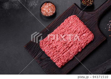 Fresh minced beef on cutting board on dark background with ingredients for cooking Fresh minced beef on cutting board on dark background with ingredients for cooking 94371510