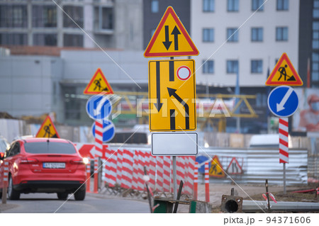 Roadworks warning traffic signs of construction work on city street and slowly moving cars Roadworks warning traffic signs of construction work on city street and slowly moving cars 94371606
