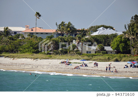 Resort beach with white sand, blue ocean water, row of comfortable hotel cottages houses under blue tropical sun Resort beach with white sand, blue ocean water, row of comfortable hotel cottages houses under blue tropical sun 94371610