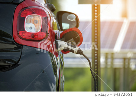 Electric plug-in car charging with electricity from solar renewable power source parked on city street 94372051