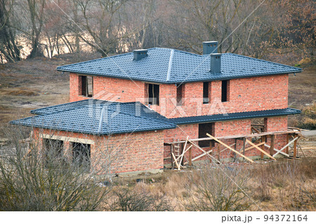 Brick house with roof top covered with metallic shingles. Tiled covering of building under construction Brick house with roof top covered with metallic shingles. Tiled covering of building under construction 94372164