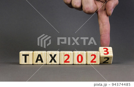 2023 tax new year symbol. Businessman turns a wooden cube and changes words Tax 2022 to Tax 2023. Beautiful grey table grey background, copy space. Business 2023 tax new year concept. 94374485