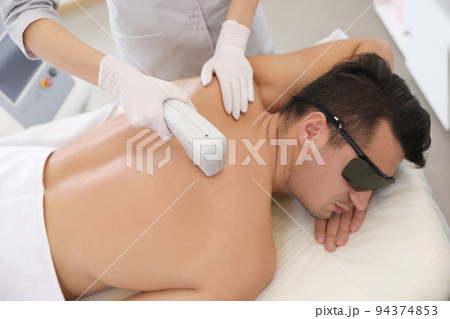 Young man undergoing laser epilation procedure in beauty salon 94374853