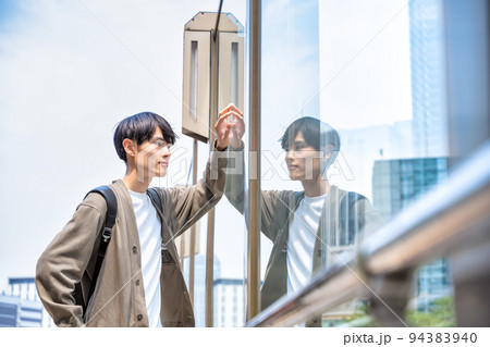 オフィスカジュアルの若いビジネスマン　新橋駅前　寄りかかる 94383940