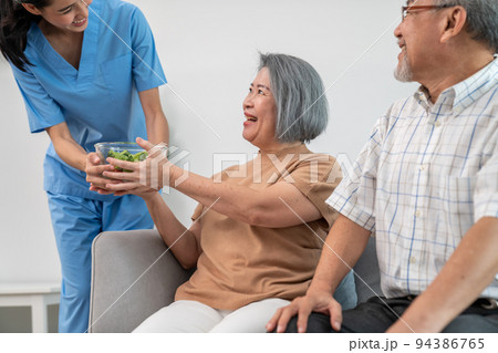A female nurse serves a bowl of salad to a contented senior couple. 94386765