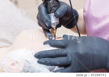 The master applies eyebrow makeup paint to the client with a tattoo machine. The master applies eyebrow makeup paint to the client with a tattoo machine. 94389741