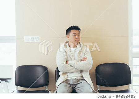 young asian man waiting for an interview or meeting sitting in the hallway in the waiting room. Student or entrant in the reception for exam or employment hr. Male patient in office a hospital clinic 94393485