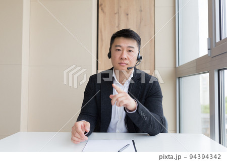 young asian male businessman talking online on video call, conference or meeting looking at camera. Webcam view. Asia Man in business suit indoors. Office negotiations distance Consultation or advice 94394342
