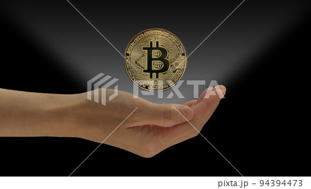 One hand holds the Bitcoin BTC, the famous cryptocurrency, with a light coming out of the hand. Black in the background 94394473
