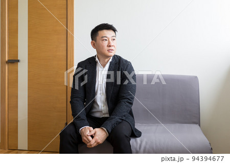 Young successful Asian man, waiting for a job interview, in the waiting room of the office center, sitting on a chair near the reception of the office center 94394677