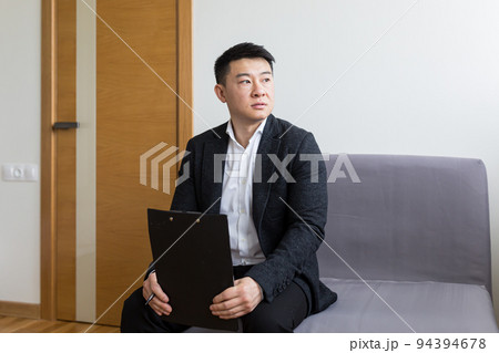 Young successful Asian man, waiting for a job interview, in the waiting room of the office center, sitting on a chair near the reception of the office center 94394678