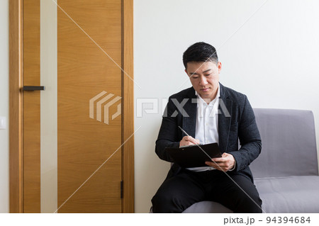 Young successful Asian man, waiting for a job interview, in the waiting room of the office center, sitting on a chair near the reception of the office center 94394684