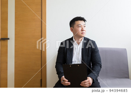 Young successful Asian man, waiting for a job interview, in the waiting room of the office center, sitting on a chair near the reception of the office center 94394685