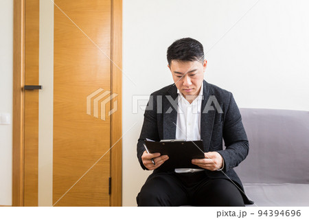 Young successful Asian man, waiting for a job interview, in the waiting room of the office center, sitting on a chair near the reception of the office center Young successful Asian man, waiting for a job interview, in the waiting room of the office center, sitting on a chair near the reception of the office center 94394696