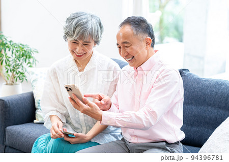リビングでスマホを見るシニア夫婦 94396781