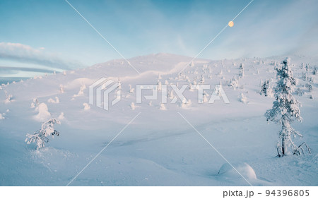Panoramic view of a winter snow-covered slope with a full moon. Arctic harsh nature. Mystical fairy tale of the winter frost forest. Panoramic view of a winter snow-covered slope with a full moon. Arctic harsh nature. Mystical fairy tale of the winter frost forest. 94396805