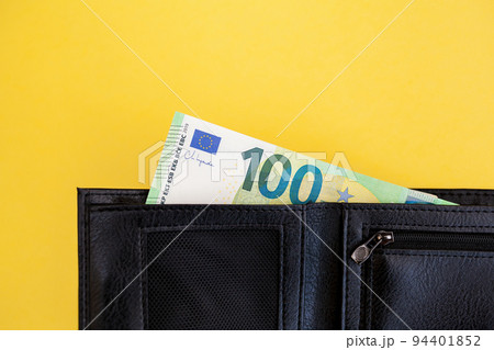 A hundred euro banknote sticks out of a black wallet on a yellow background. cash paper currency, payment, earning and savings, european currency, money and finance concep. space for text A hundred euro banknote sticks out of a black wallet on a yellow background. cash paper currency, payment, earning and savings, european currency, money and finance concep. space for text 94401852