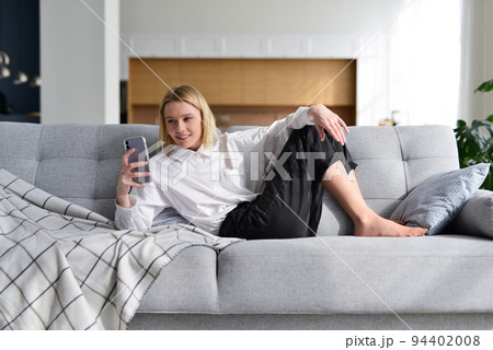 Woman with smartphone at home lying on sofa Woman with smartphone at home lying on sofa 94402008