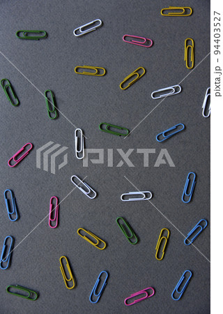 Multicolored iron paper clips on a gray background. Stationery paper fasteners scattered on a gray background like stars. 94403527