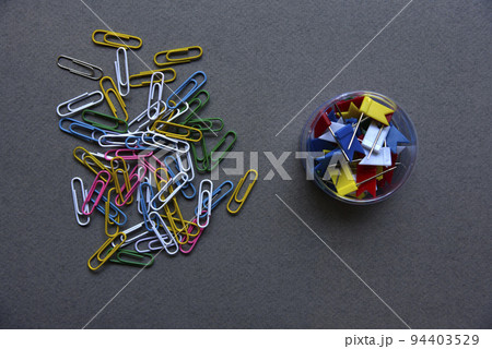 Multicolored paper clips on a gray background and in a jar. Paper clips on a gray background. 94403529