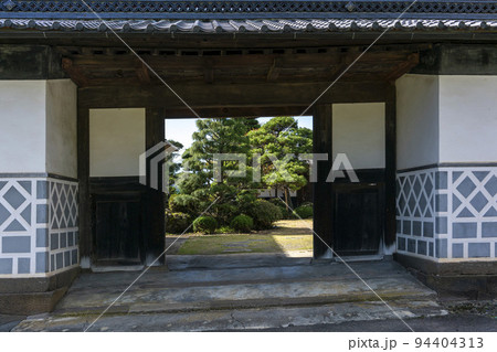 漆喰の大きな門構えの奥に日本庭園が見える民家 94404313