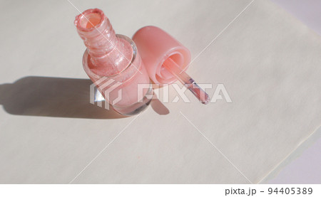 An open bottle with pink nail polish and a brush next to it on a white surface with a shadow, the concept of fashionable beauty 94405389