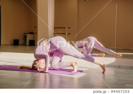 View from above. A beautiful young woman in pink sportswear is engaged in yoga, sports in the hall on a purple rug. Yoga, sport and healthy concept. 94407203