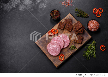 Delicious fresh smoked sausage cut with slices on a wooden cutting board Delicious fresh smoked sausage cut with slices on a wooden cutting board 94408695