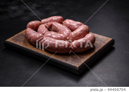 Raw barbecue sausages on a wooden cutting board with spices and herbs 94408704