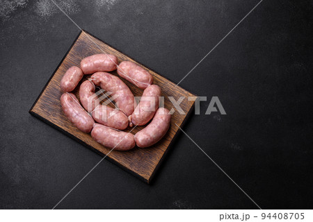 Raw barbecue sausages on a wooden cutting board with spices and herbs 94408705