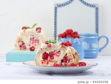 Baked meringue roll with cream and fresh red raspberry, white background. 94409296