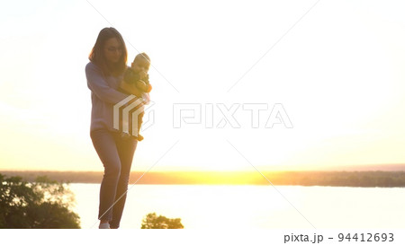 A young mother in glasses holds her son in her arms at sunset. Walk in the nature of a woman with a child. A young mother in glasses holds her son in her arms at sunset. Walk in the nature of a woman with a child. 94412693