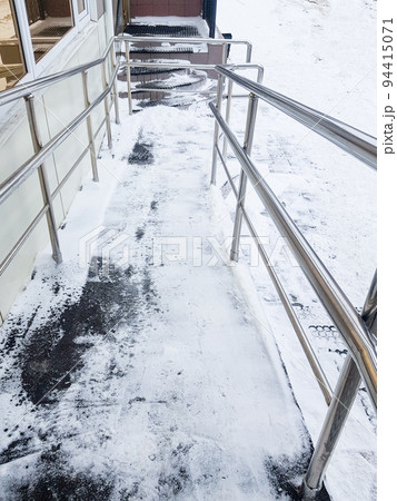 Modern ramp with metal railings for accessible movement of people with disabilities, ramp covered with snow, top view, vertical photo 94415071