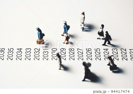 年表の横を歩くミニチュアの人々 94417474